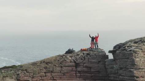 A picture of Jesse and Molly, with one arm around each other and the other arm in the air on top of the old man of hoy. Alastair is in shot, filming our celebration.