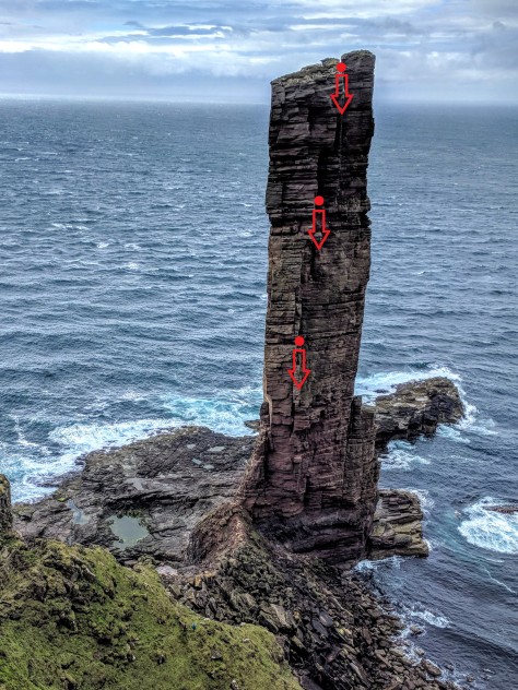 A picture showing the old man of hoy with the sea in the background. Red arrows have been drawn at 3 points on the sea stack to show where the abseil points are.