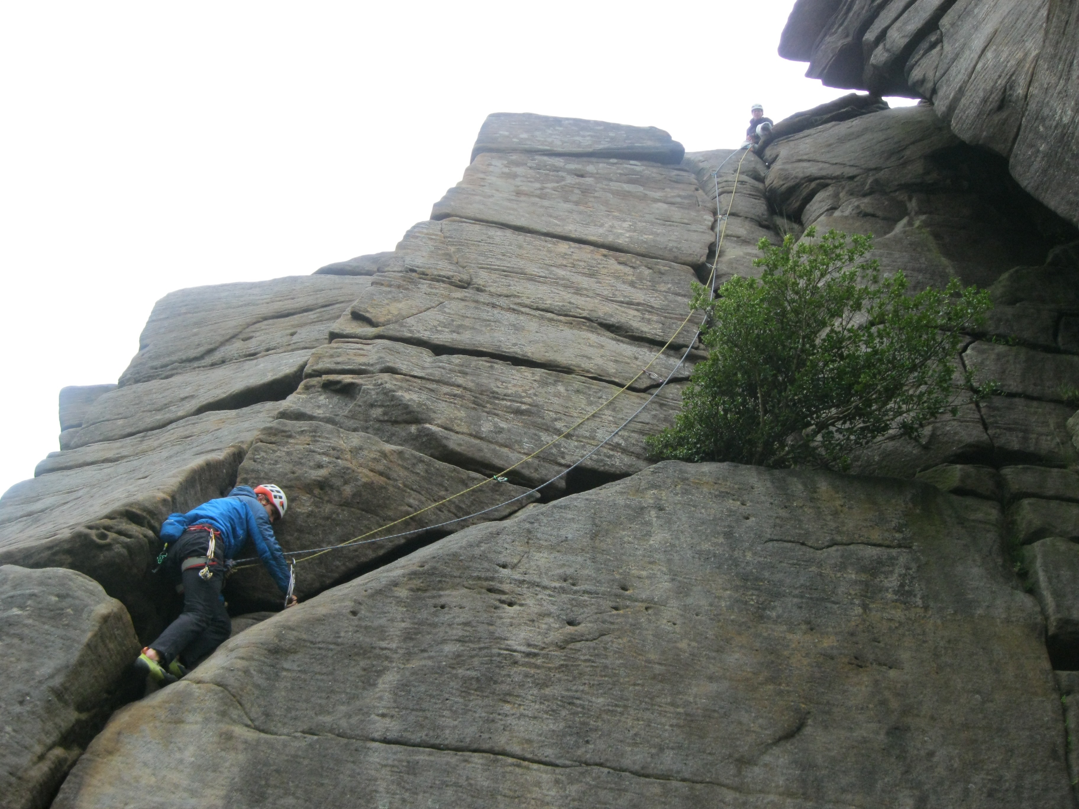 A picture of Molly sat at the top of the crag and Jesse climbing the route  on second.