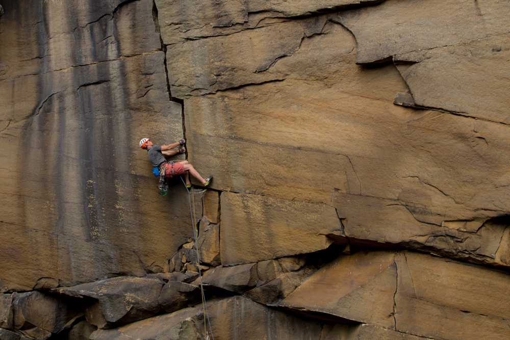 Jesse climbing Forked Lightning Crack E2 5c, Yorkshire, UK. The picture shows Jesse laybacking to the left in the middle of a lightning shaped cracked that splits the crag vertically. He is wearing shorts, what was he thinking.