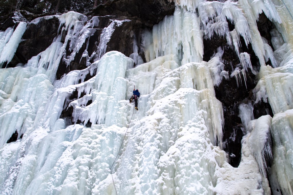 A picture of Jesse ice climbing on a huge frozen waterfall in Norway. He is leading up with the rope below him, and swinging his axe into the ice. The ice has formed in hanging chandeliers which looks quite spectacular. 