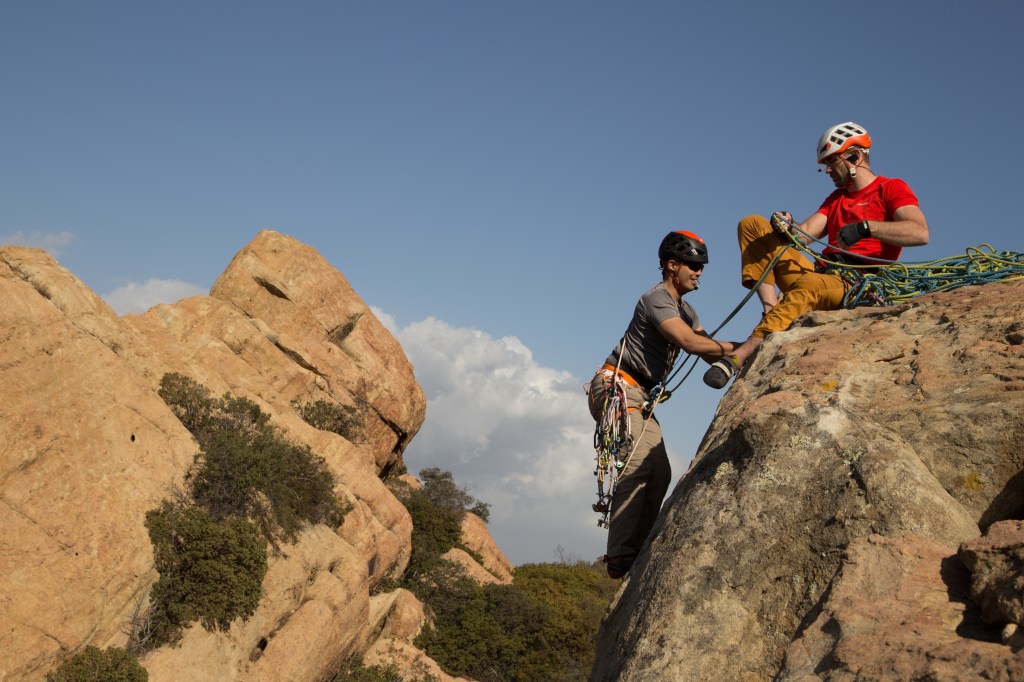 A photo of Jesse sat on top of the crag and Justen climbing up just below him on second. 