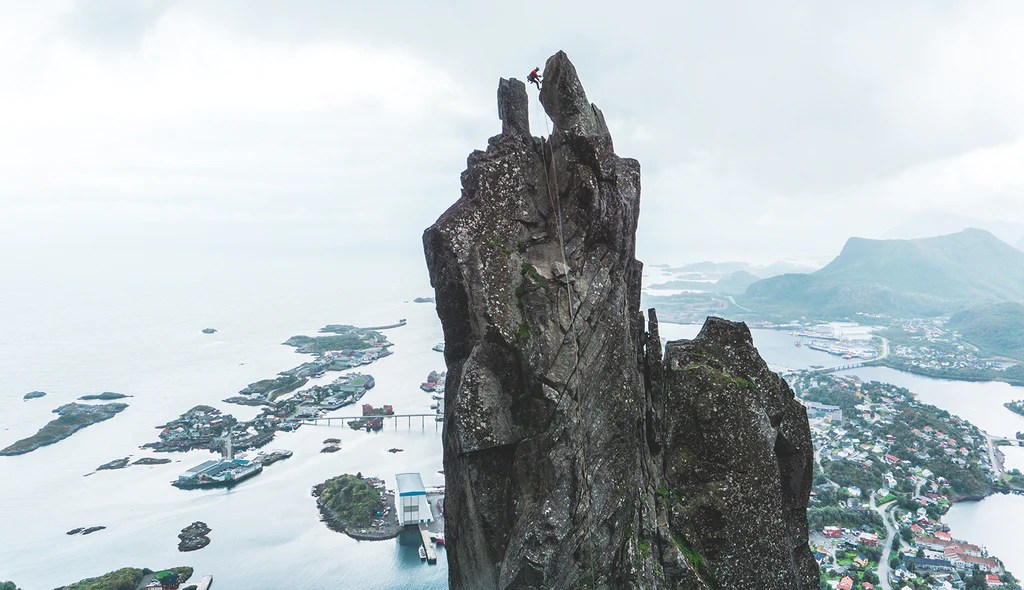A photo of the goat, with Jesse abseiling off the Goat with Svolvaer town and the sea in the background.