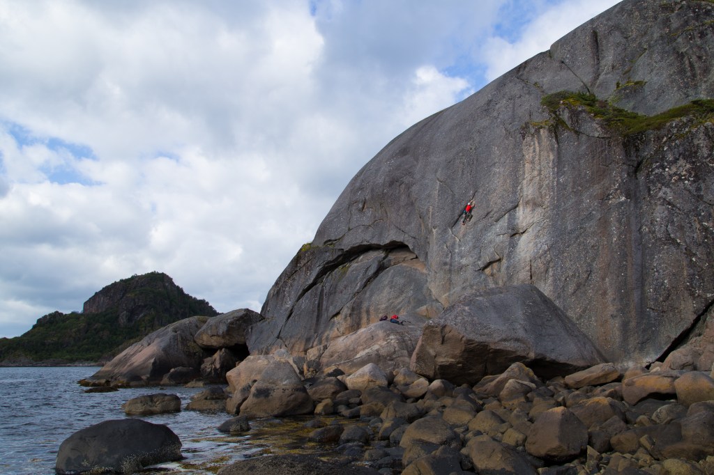 A photo of Jesse climbing up a smooth slab, next to the sea. 