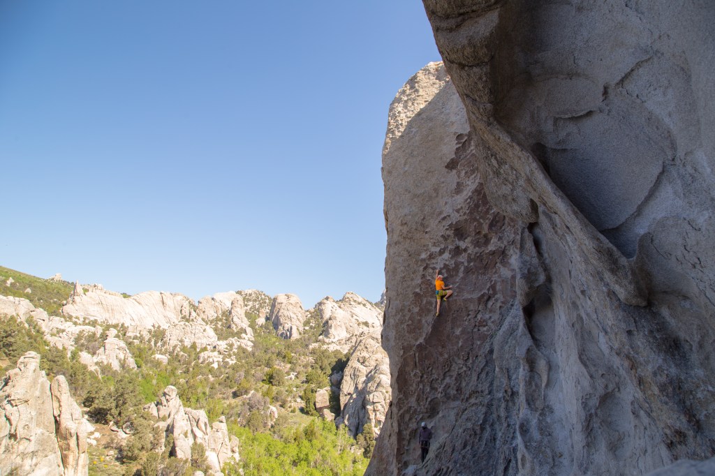 A photo showing Jesse half way up Tribal Boundaries. A impecible sheet of steep rock covered in small patina edges.