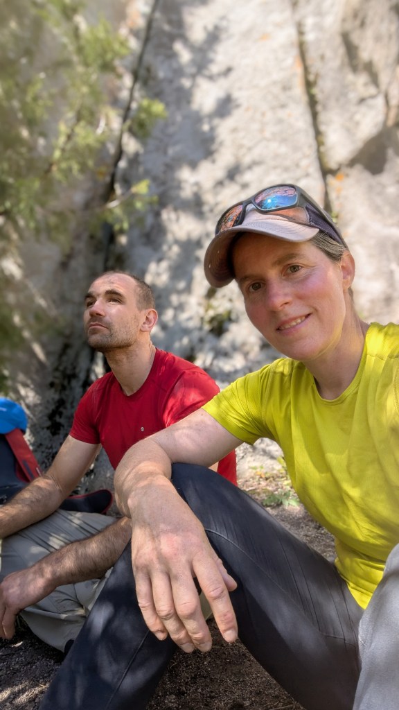 A photo of Molly and Jesse sat in the shade at the bottom of a crag.