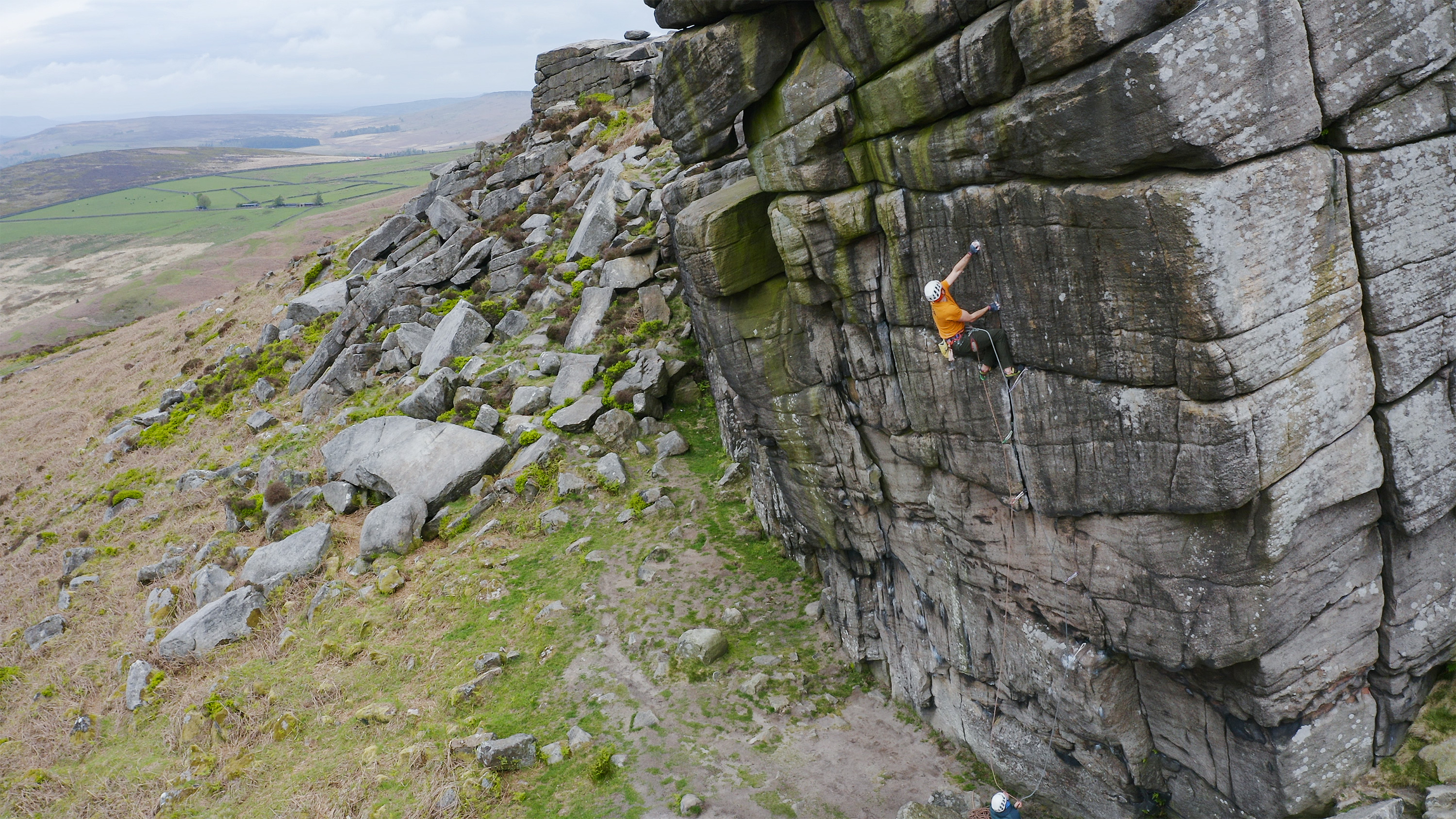 A photo of Jesse holding on to a small hold with his left hand geting ready to pounce up for the large sloping break.